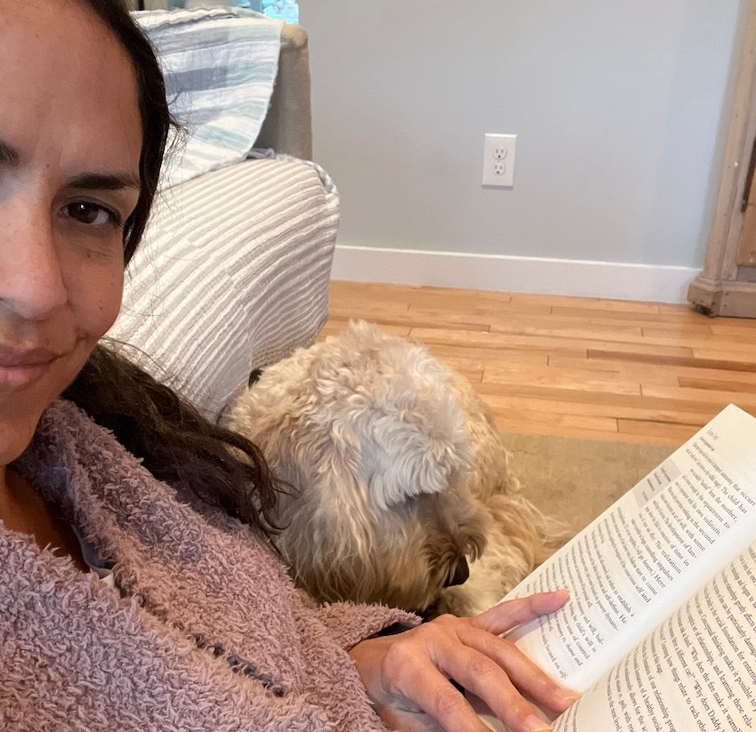 Female sitting next to her Goldendoodle while reading