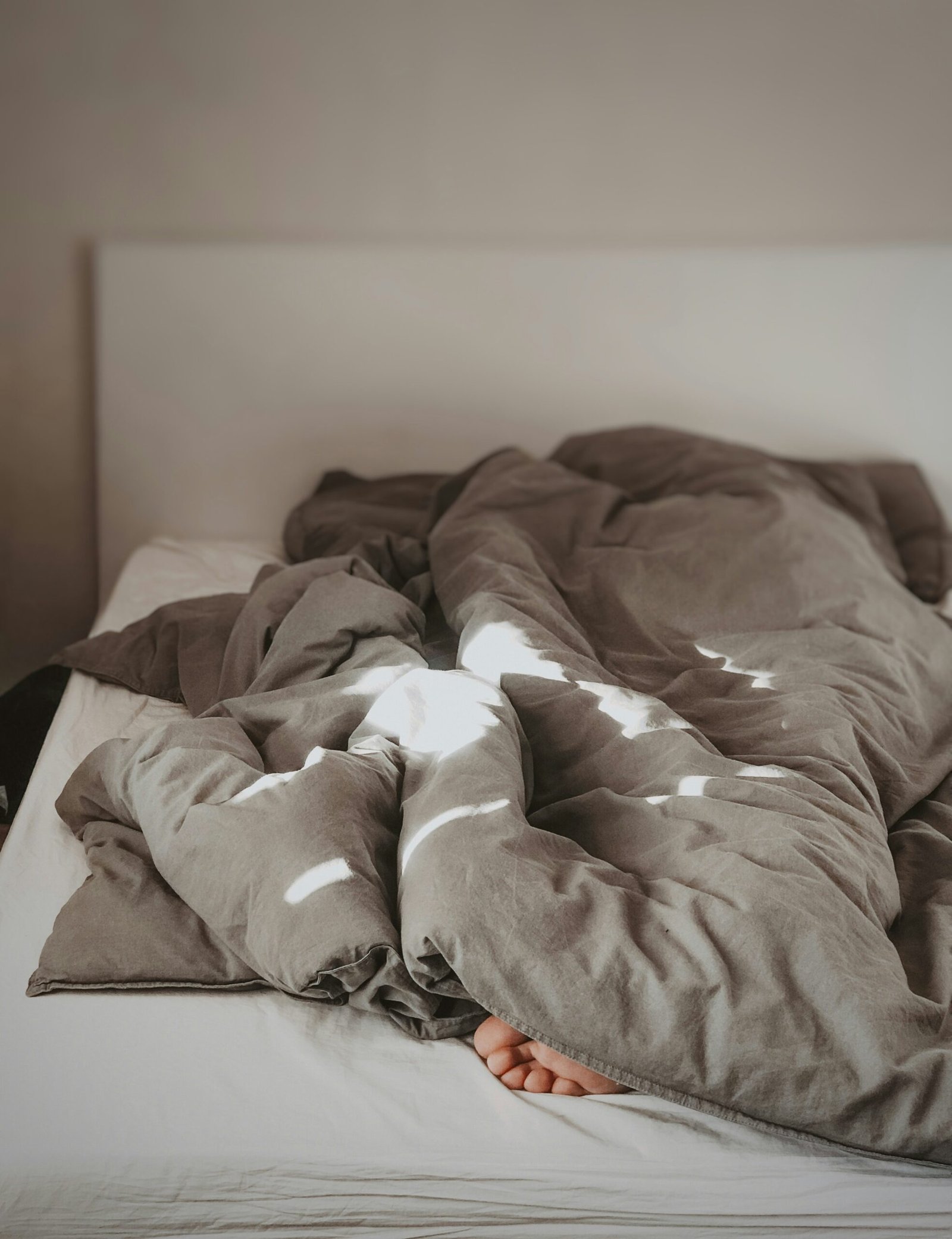A female is trying to sleep under the bedcovers.