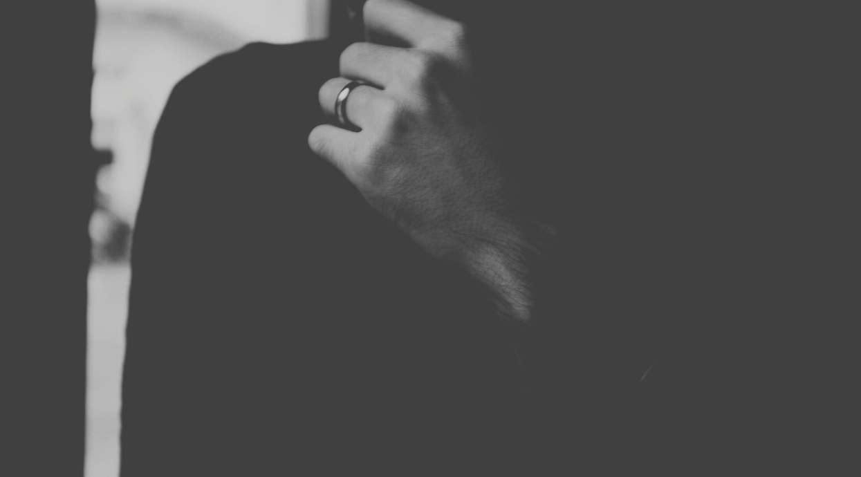 A black and white image of a man leaning on elbow with hand under chin, thinking.